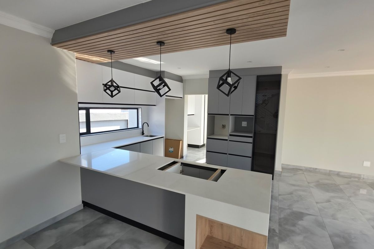 Modern kitchen featuring sleek cabinetry, a central island with quartz countertops, and stylish pendant lighting, awaiting final appliance installation.