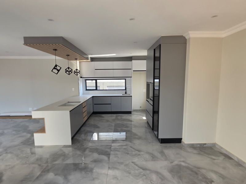 Modern, newly renovated kitchen featuring sleek grey and white cabinetry, a large island with stone countertops, and polished marble-look tiled flooring.