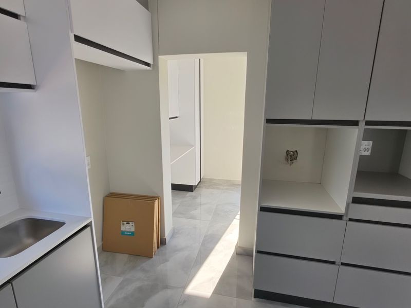 A modern, minimalist kitchen featuring grey cabinetry, stone countertops, an undermount sink with a black mixer tap, and light-toned tiled flooring.