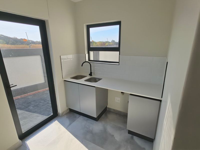 A modern, clean scullery featuring a double sink, black mixer tap, subway tile splashback, and sleek built-in cabinetry with stone countertops.