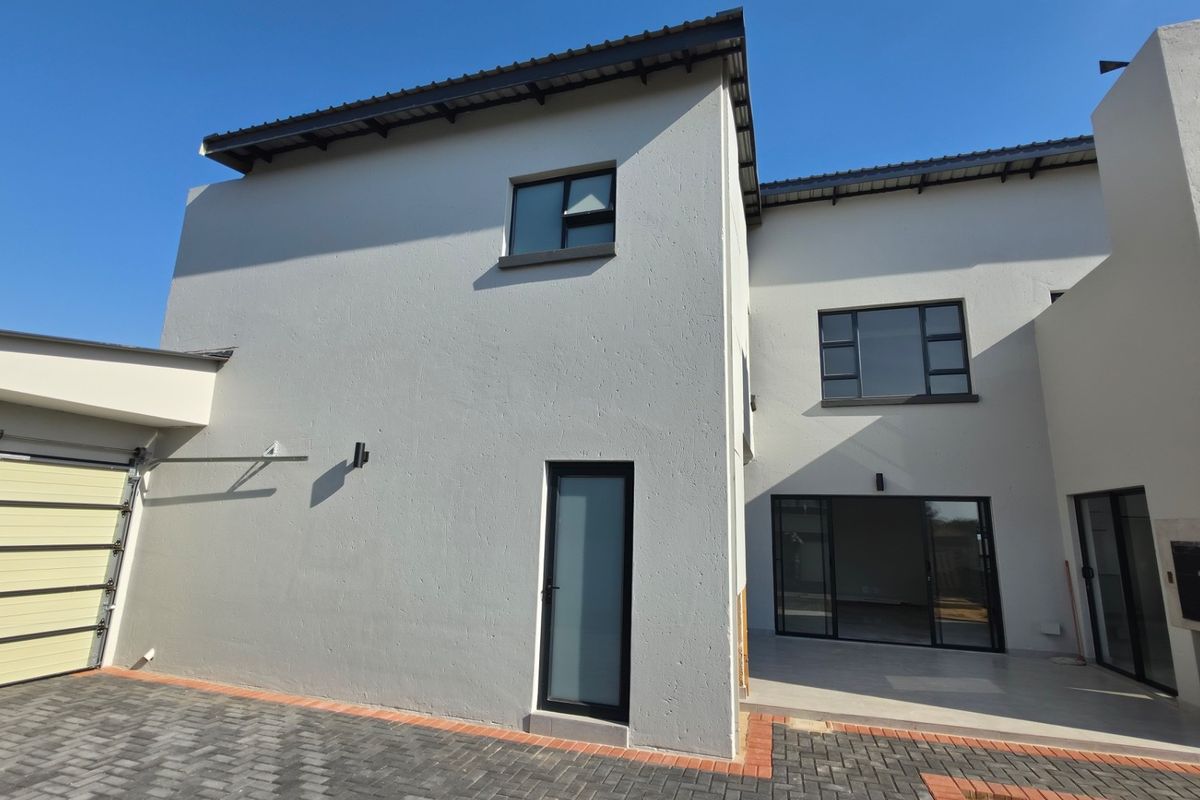 Rear view of a modern double-storey home featuring a paved driveway, garage, tiled patio area, and a built-in outdoor braai.