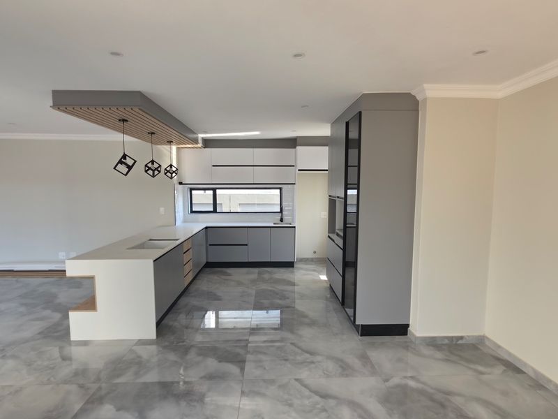 Modern, open-plan kitchen featuring sleek grey and white cabinetry, a central island with integrated sink, and polished marble-look tiled flooring.