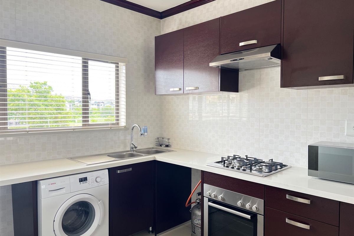 A functional kitchen featuring dark wood cabinetry, a built-in gas hob, oven, extractor fan, and a double sink with a window view.