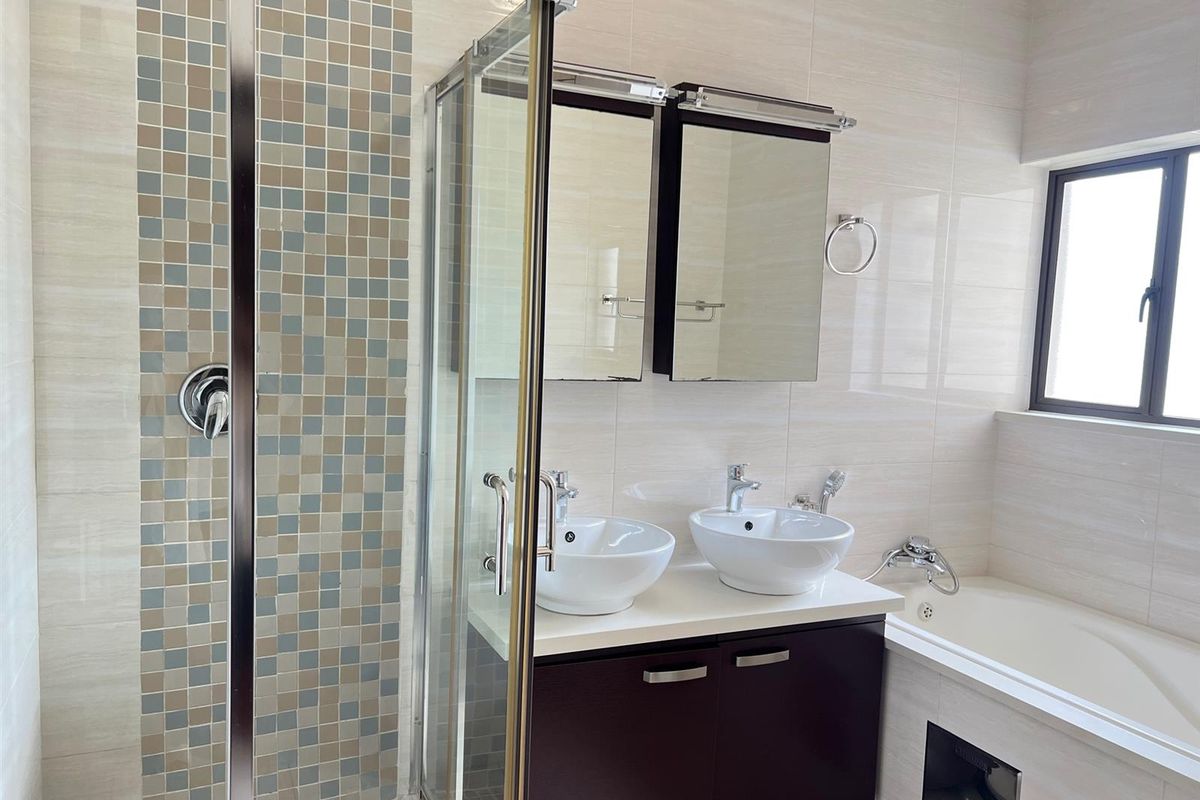Modern bathroom featuring a glass-enclosed shower, double vanity with vessel sinks, and a built-in bathtub with neutral wall tiling.