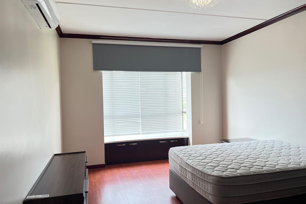 A well-maintained bedroom featuring dark wood flooring, a built-in window seat with storage, and a wall-mounted air conditioning unit.