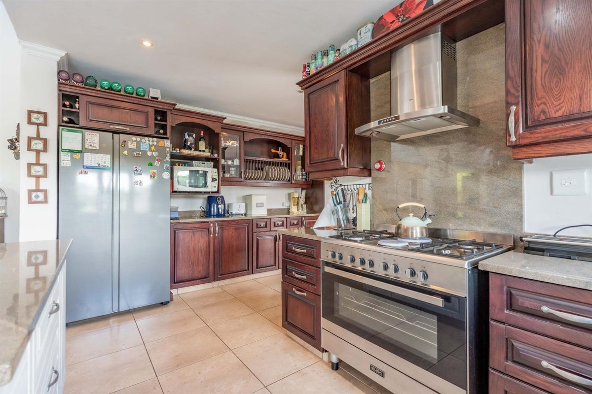 A functional kitchen featuring dark wood cabinetry, stone-look countertops, tiled flooring, and a stainless steel gas stove with an integrated extractor fan.