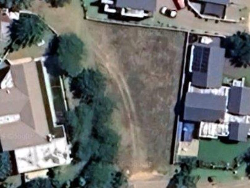 An aerial view of a vacant residential plot situated between existing developed properties in a suburban neighborhood.