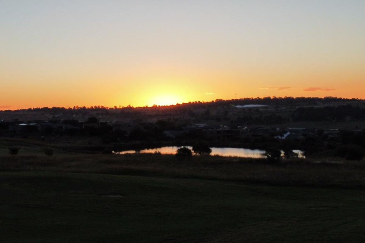 A scenic sunset view overlooking a natural landscape with a small pond and distant horizon.