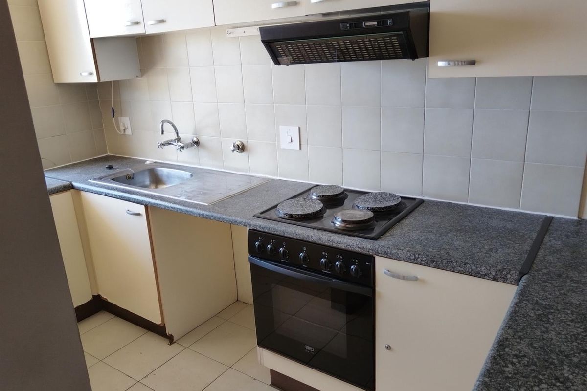 A functional kitchen featuring laminate countertops, a built-in oven with electric hob, extractor fan, and tiled splashbacks with ample cabinetry.