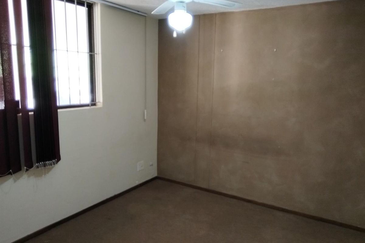 An empty bedroom featuring carpet flooring, a ceiling fan with integrated light, and a window with security bars.
