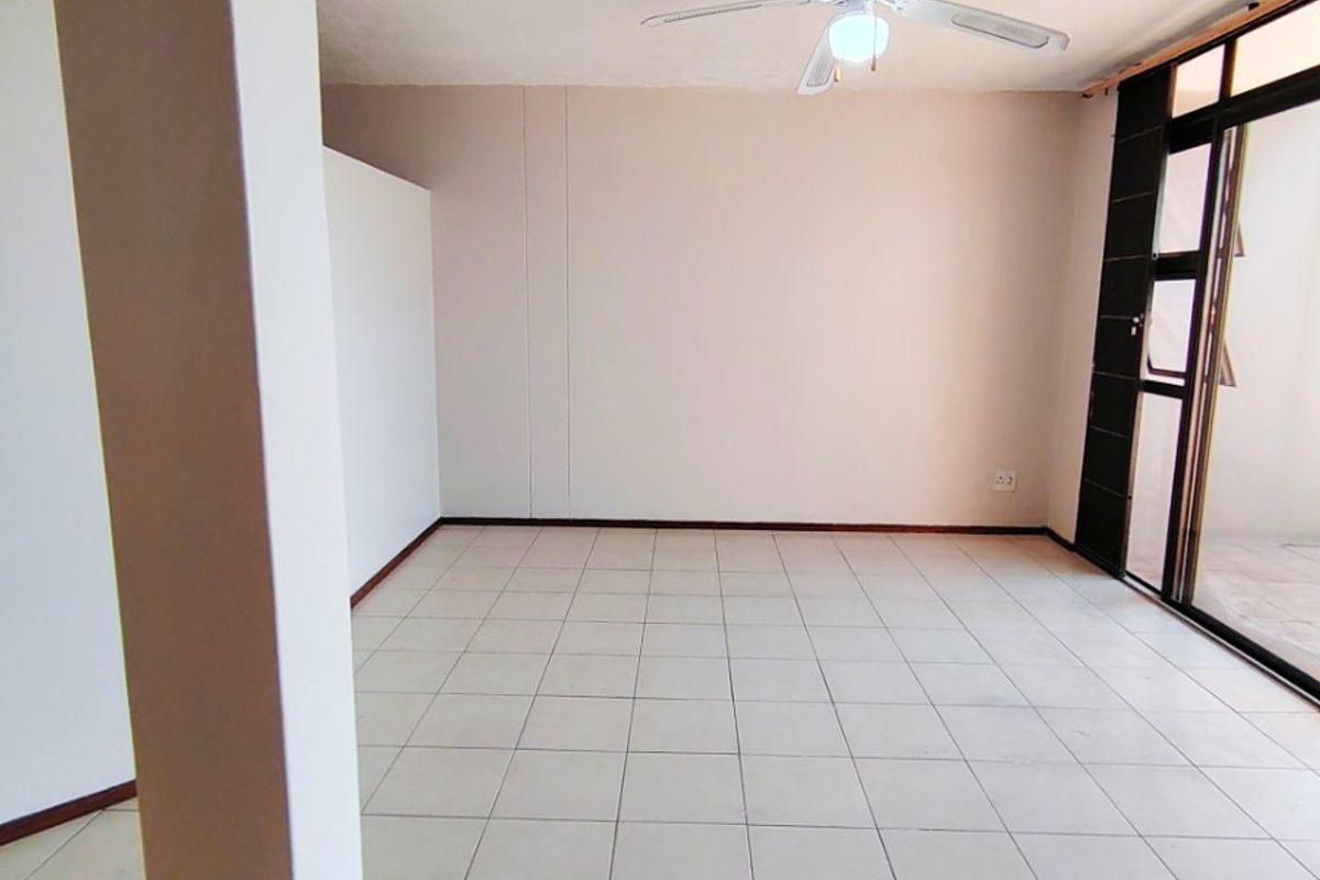 An empty, open-plan living area featuring neutral tiled flooring, a ceiling fan, and large sliding glass doors providing access to an outdoor space.