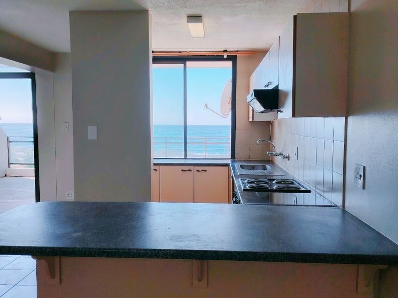 Open plan kitchen area featuring built-in cabinetry, a breakfast counter, and direct access to a balcony with ocean views.
