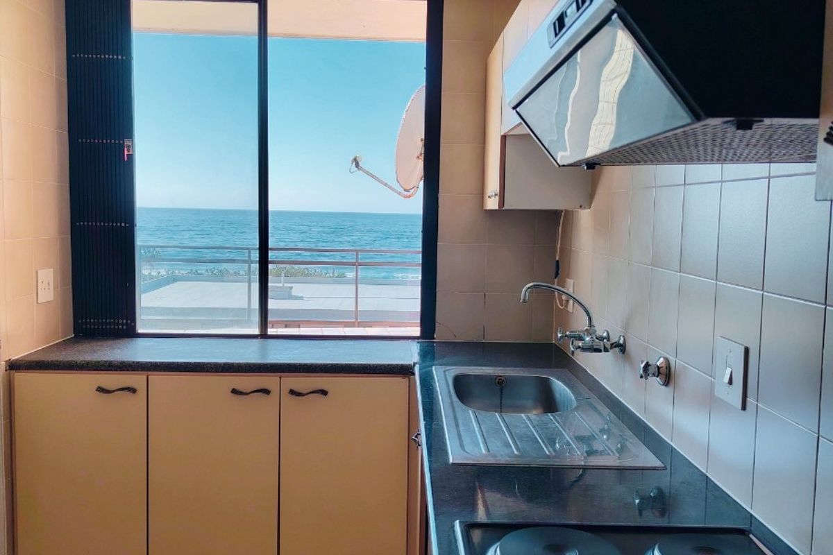 A functional kitchen featuring built-in cabinetry, a stainless steel sink, and an electric hob, offering a direct view of the ocean.