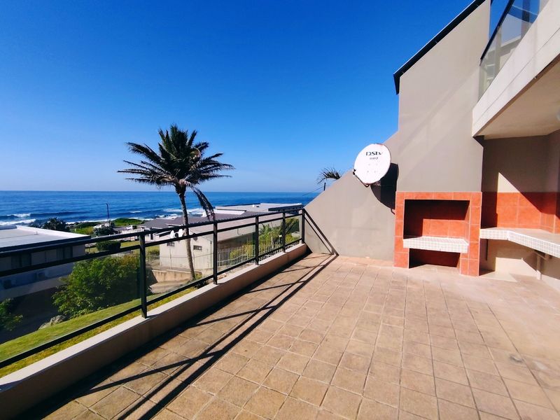 Spacious balcony featuring a built-in braai, tiled flooring, and a glass balustrade, offering expansive ocean views.