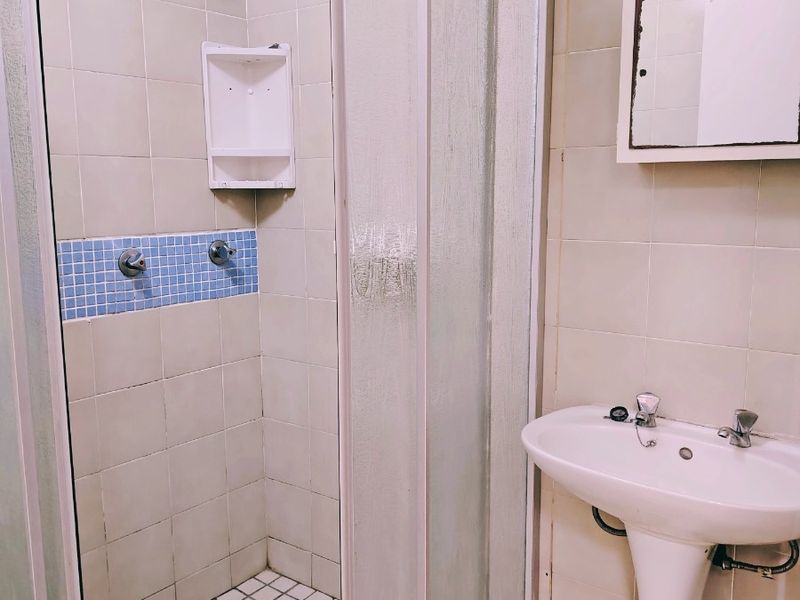A functional bathroom featuring a shower enclosure with tiled walls and a pedestal basin, currently in need of cosmetic updates.