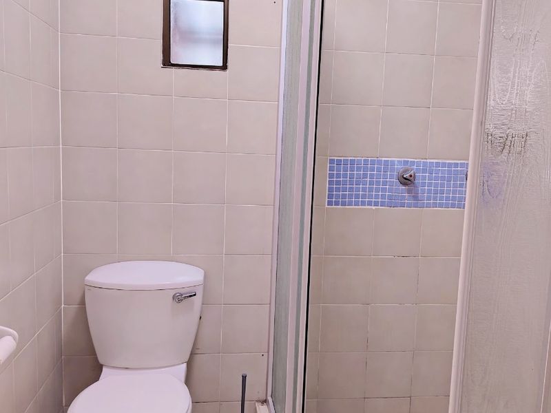 Compact bathroom featuring a tiled shower enclosure, standard toilet, and neutral wall tiling, offering a functional space ready for modernization.