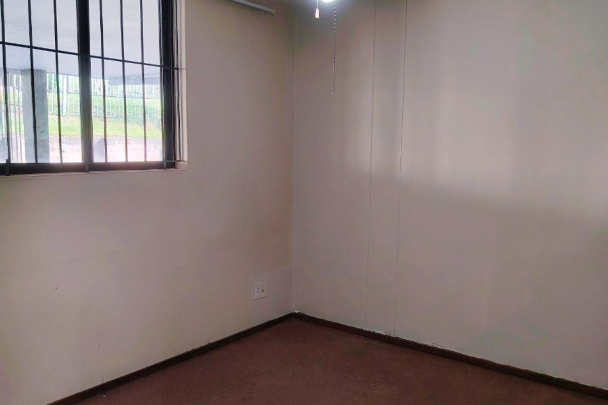 An empty bedroom featuring carpet flooring, a ceiling fan, and security bars on the window, providing a blank canvas for potential updates.