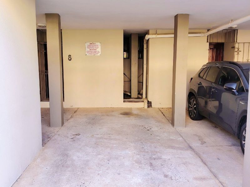 A covered parking bay featuring concrete flooring and structural support columns, providing dedicated off-street parking for the apartment unit.