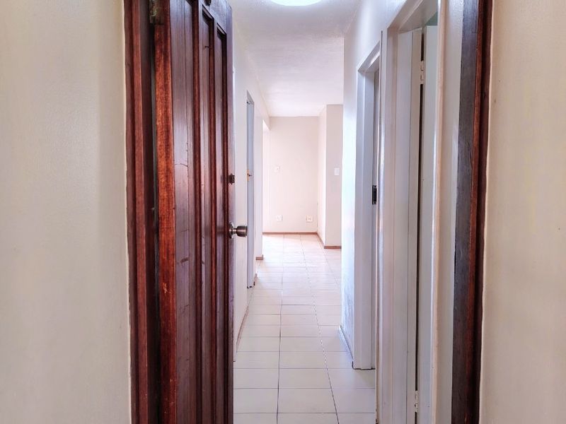 A functional hallway featuring tiled flooring, a flush mount ceiling light, and traditional wooden door frames connecting the apartment spaces.
