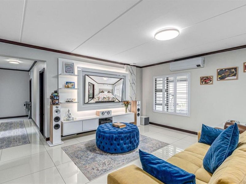 Modern living room featuring a custom built-in media unit with integrated lighting, tiled flooring, and a wall-mounted air conditioning unit.
