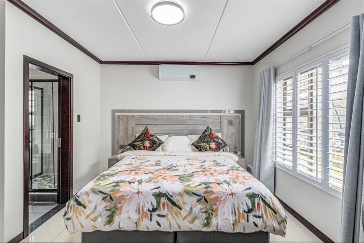A well-maintained bedroom featuring tiled floors, a built-in headboard, split-system air conditioning, and shutter blinds, with an adjoining en-suite bathroom.