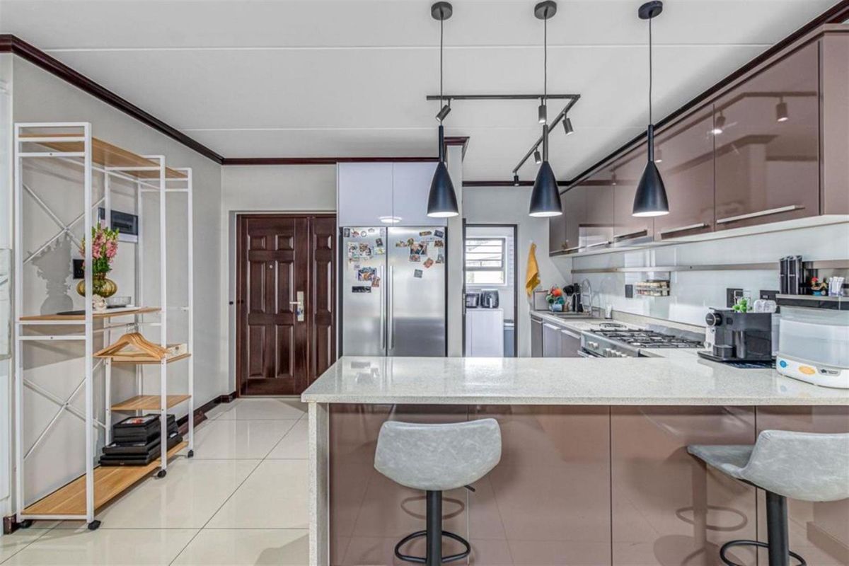 Modern kitchen featuring high-gloss cabinetry, stone countertops, gas hob, and integrated lighting, with an open-plan layout and tiled flooring.