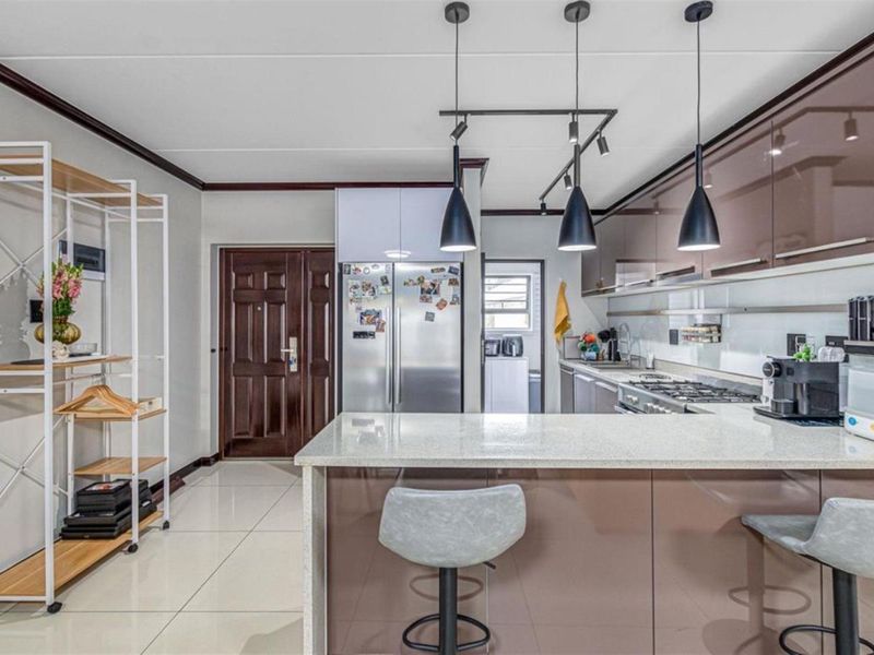 Modern kitchen featuring high-gloss cabinetry, stone countertops, gas hob, and integrated lighting, with an open-plan layout and tiled flooring.