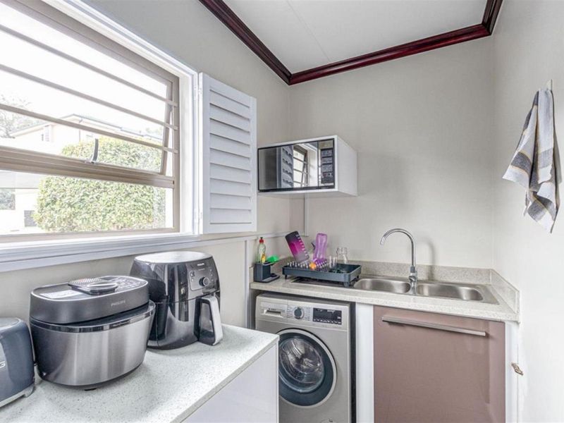Compact laundry area featuring a stainless steel double sink, stone-look countertops, built-in cabinetry, and window security bars.