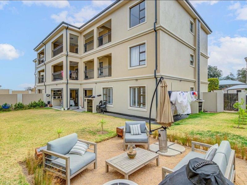 Rear view of a multi-story apartment building featuring private balconies, landscaped garden area, and secure boundary walling.