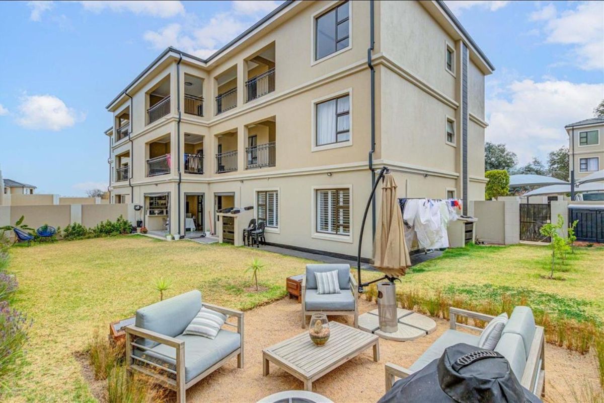 Rear view of a multi-story apartment building featuring private balconies, landscaped garden area, and secure boundary walling.