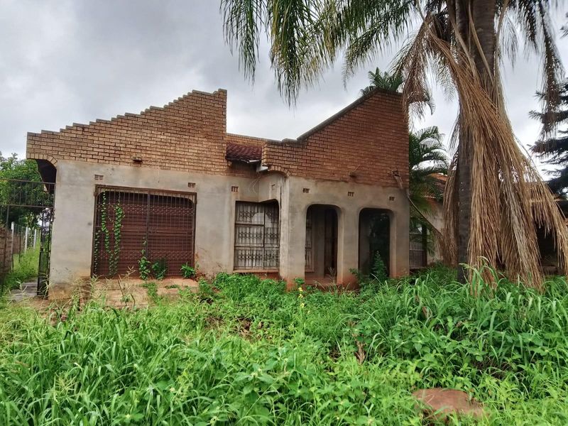 Front elevation of a house in poor condition, featuring exposed brickwork, missing roof sections, and significant overgrowth requiring extensive renovation.