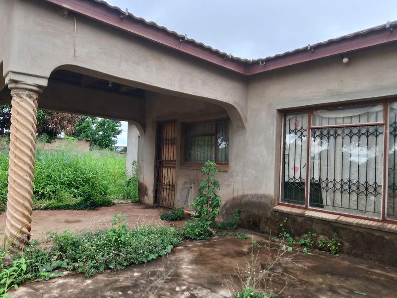 Rear exterior view of the house featuring a covered patio area with a decorative column, requiring maintenance and landscaping.
