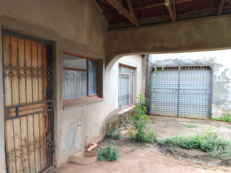 A covered outdoor patio area featuring exposed timber rafters, security gates, and concrete flooring, requiring maintenance and cosmetic updates.