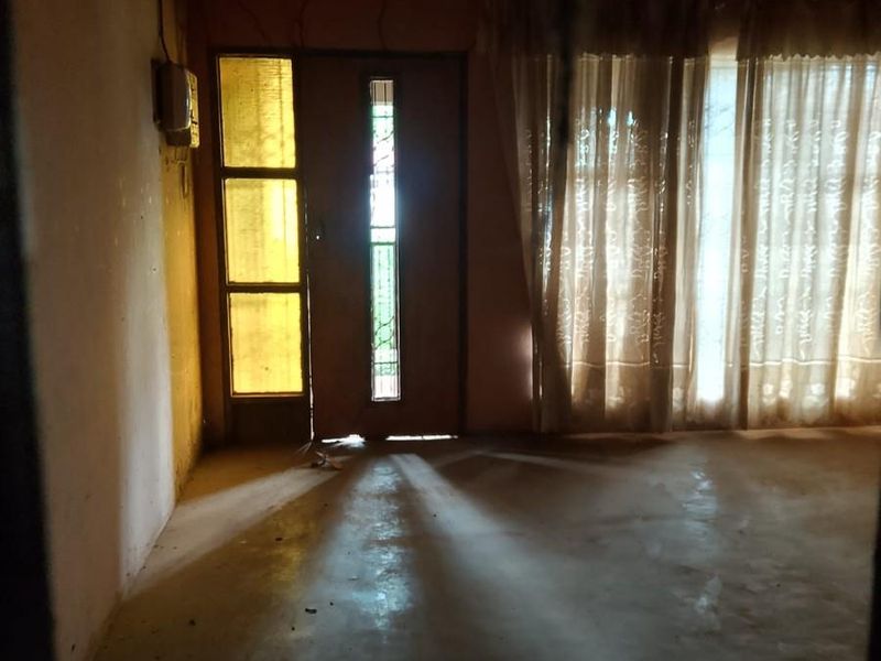 An empty living room space featuring exposed ceiling beams, a decorative leaded glass door, and large windows allowing natural light.