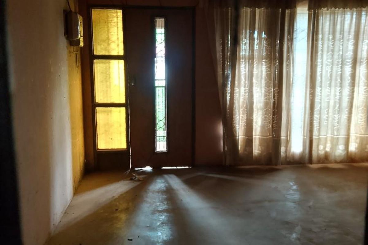 An empty living room space featuring exposed ceiling beams, a decorative leaded glass door, and large windows allowing natural light.