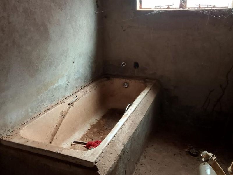 A bathroom in shell condition featuring a built-in bathtub, security bars on the window, and unfinished wall surfaces requiring complete renovation.