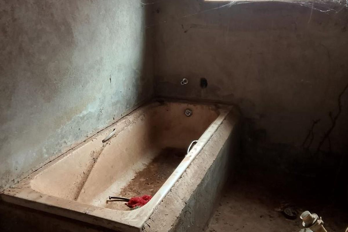 A bathroom in shell condition featuring a built-in bathtub, security bars on the window, and unfinished wall surfaces requiring complete renovation.