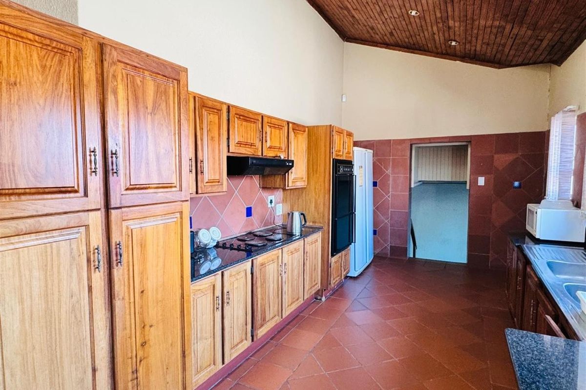 Spacious kitchen featuring extensive wooden cabinetry, dark granite countertops, built-in oven, extractor fan, and terracotta-style floor tiles with a vaulted timber ceiling.