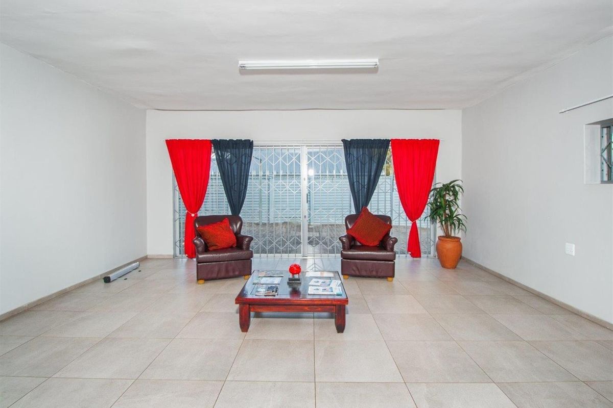A spacious living room featuring neutral floor tiles, a large sliding glass door with security gate, and a simple ceiling-mounted light fixture.