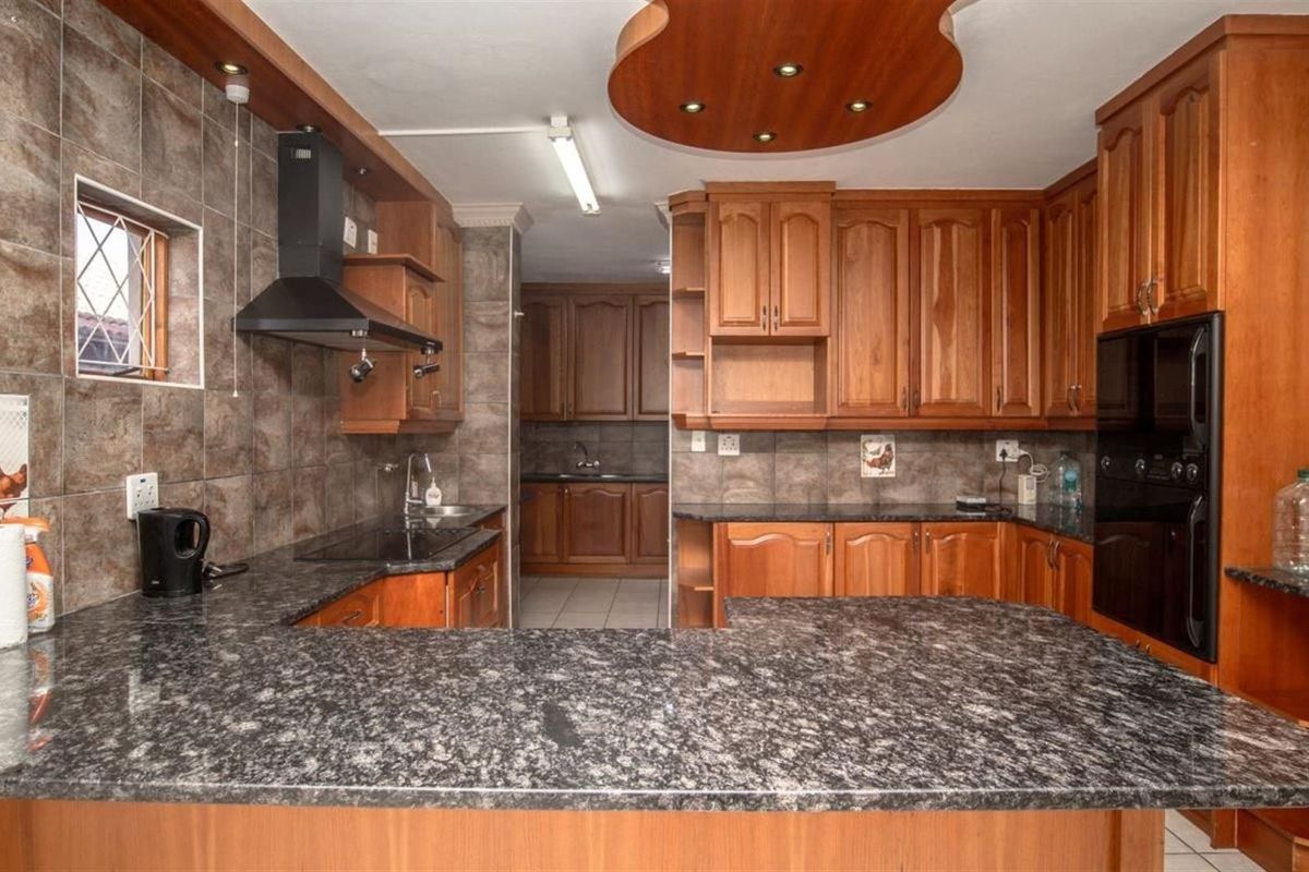 A traditional kitchen featuring extensive wooden cabinetry, granite countertops, a built-in oven, and a decorative wooden ceiling feature with recessed lighting.