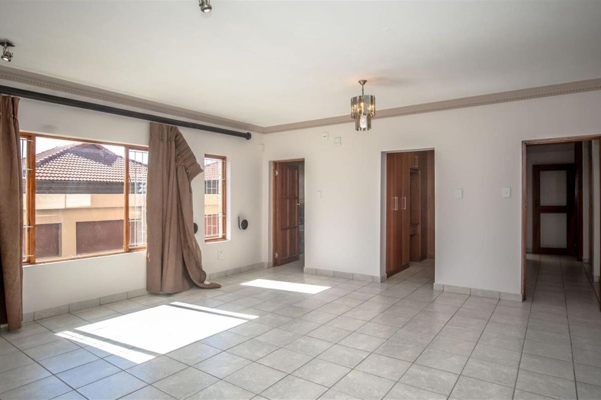 Spacious living area featuring neutral ceramic floor tiles, crown molding, and multiple wooden door frames leading to adjacent rooms.