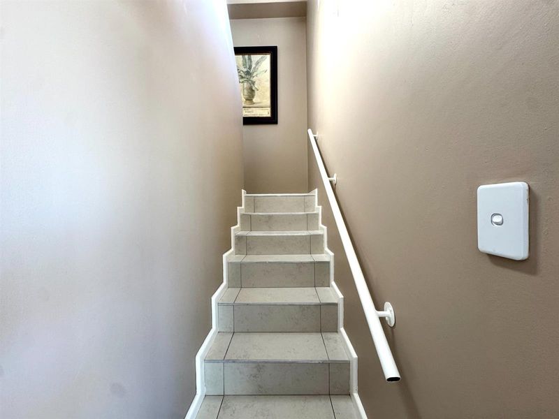 A staircase featuring tiled steps and a simple white handrail, leading to an upper level.