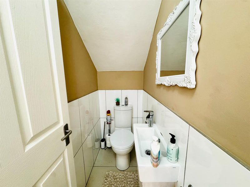 Compact guest bathroom featuring a modern toilet, wall-mounted basin with chrome faucet, and half-tiled walls under a sloped ceiling.