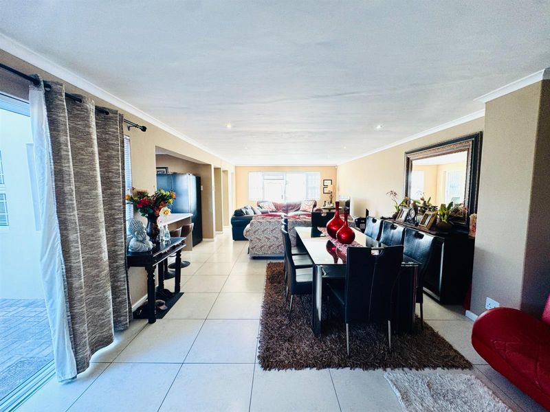 Spacious open-plan living and dining area featuring large format floor tiles, recessed downlighting, and sliding glass doors leading to the exterior.
