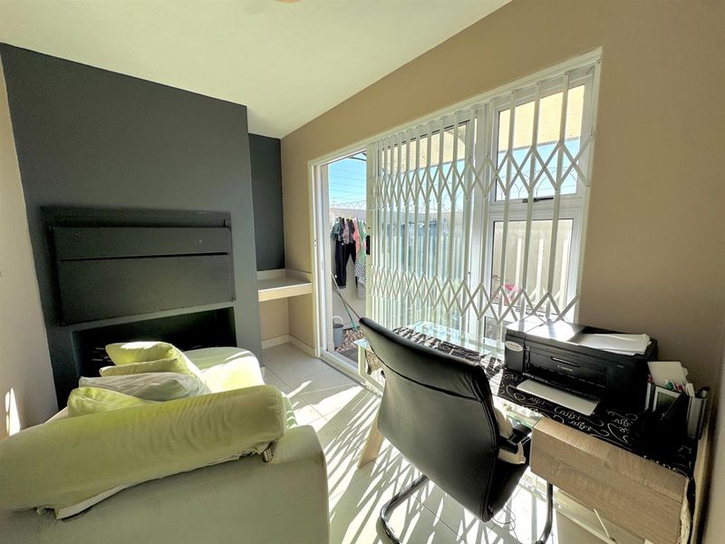 A functional office space featuring a built-in fireplace, tiled flooring, and a sliding glass door with security gate leading to an outdoor area.