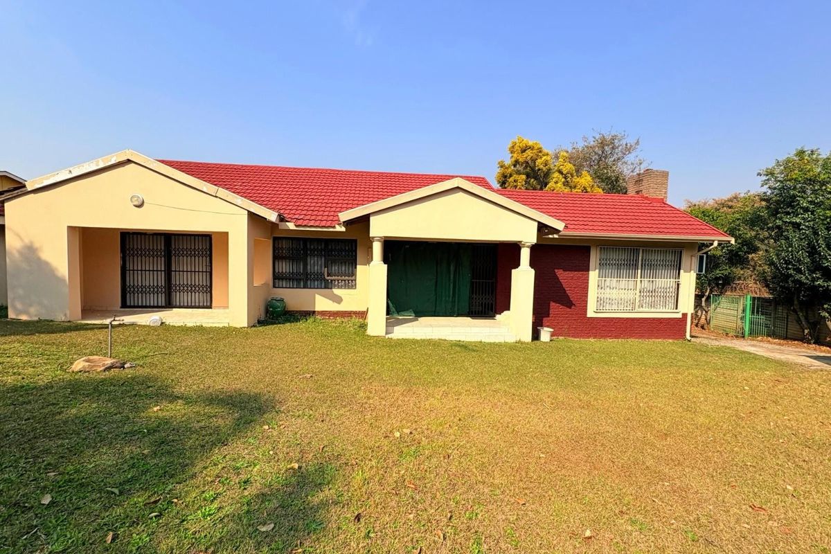 A rear view of a single-story house featuring a red tiled roof, brick and plaster facade, and a covered patio area overlooking the garden.