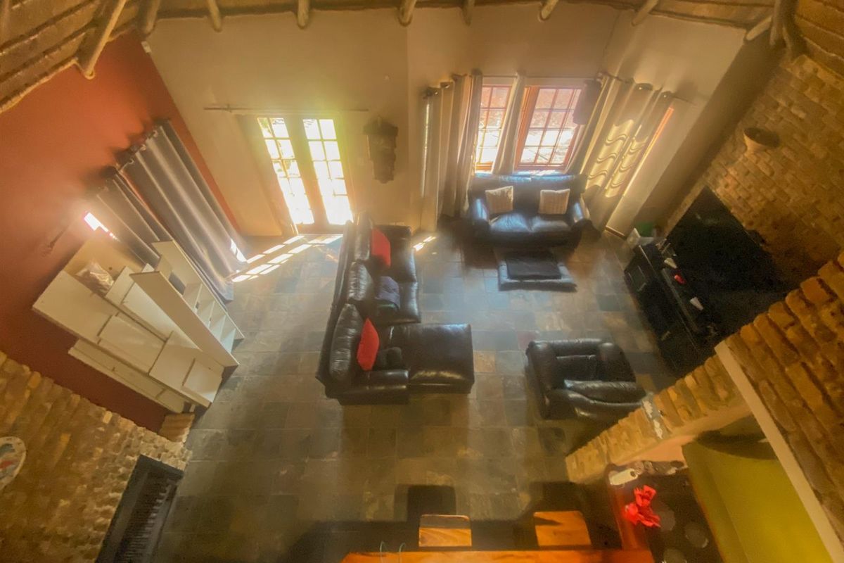 Spacious living area featuring a high thatched ceiling, exposed brickwork, slate flooring, and a built-in fireplace, creating a rustic and warm atmosphere.