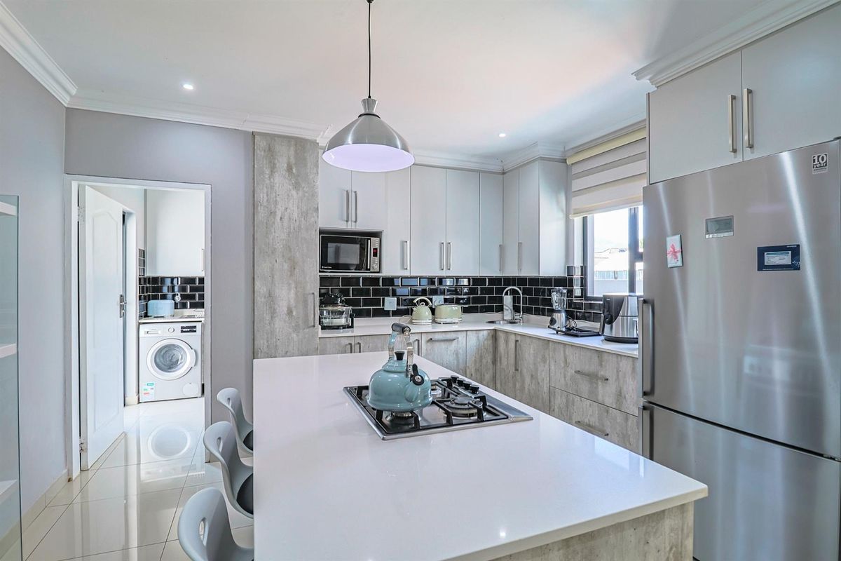 Modern kitchen featuring a central island with a built-in gas hob, sleek cabinetry, stone countertops, and an adjacent laundry area.