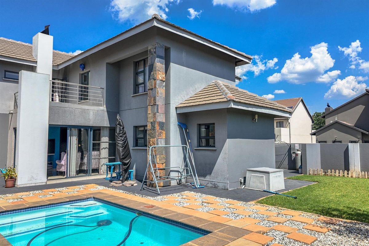 Rear view of the property featuring a swimming pool, paved patio area, and a two-story exterior facade with stone cladding accents.