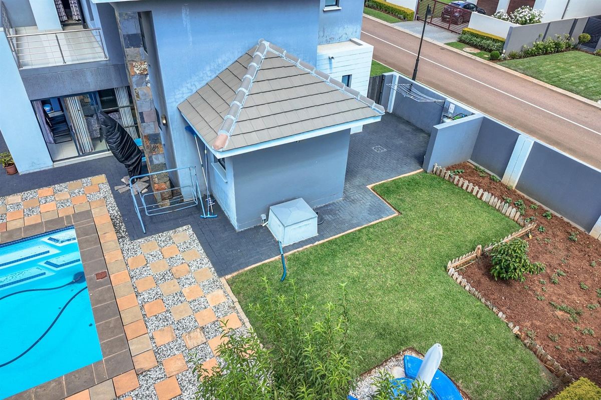 Aerial view of the property backyard featuring a swimming pool, paved patio area, small garden, and a detached structure with a tiled roof.